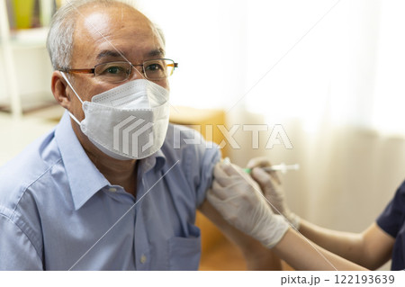 Medical worker perform a vaccine injection to senior Asian man in clinic or medical facility. Medical worker perform a vaccine injection to senior Asian man in clinic or medical facility. 122193639