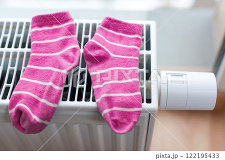Pink striped socks drying on a home radiator with a modern thermostat. Warmth, domestic comfort, and energy efficiency. 122195433