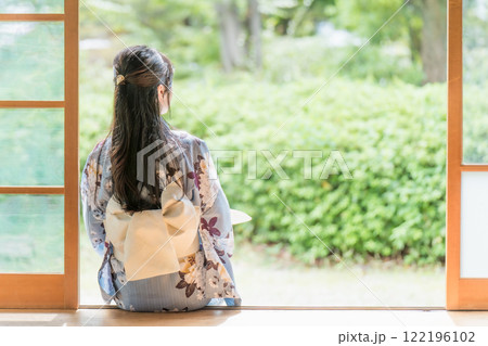 古民家の縁側に座って、団扇で扇いで涼む若い女性 122196102