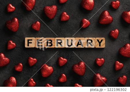 Word February in English from wooden blocks on a dark background with red glittery hearts 122196302