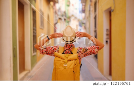 Woman in dress strolls through colorful streets of Spanish coastal town of La Vila Joiosa . sunny winter atmosphere highlights charm of Mediterranean architecture and quiet seaside life, back view Woman in dress strolls through colorful streets of Spanish coastal town of La Vila Joiosa . sunny winter atmosphere highlights charm of Mediterranean architecture and quiet seaside life, back view 122196761
