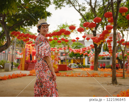 Young woman in ethnic dress and hat exploring the festive streets of George Town, Malaysia, Chinese New Year. Vibrant lanterns, cultural celebrations, and historic charm create a unique atmosphere. 122196845