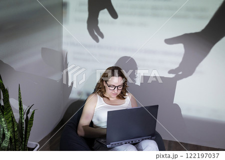 A woman works on her laptop, with shadows symbolizing digital threats around her A woman works on her laptop, with shadows symbolizing digital threats around her 122197037