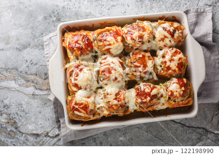 Homemade baked sliders stuffed with meatballs, topped with tomato sauce and grated cheese close-up in a baking dish. horizontal top view Homemade baked sliders stuffed with meatballs, topped with tomato sauce and grated cheese close-up in a baking dish. horizontal top view 122198990