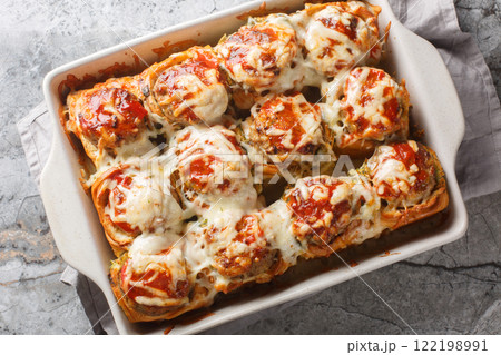 Hot sandwiches made from dinner rolls filled with meatballs, topped with tomato sauce and sprinkled with cheese close-up in a baking dish. horizontal top view Hot sandwiches made from dinner rolls filled with meatballs, topped with tomato sauce and sprinkled with cheese close-up in a baking dish. horizontal top view 122198991