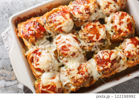 Baked dinner rolls stuffed with meatballs, topped with tomato sauce and sprinkled with cheese close-up in a baking dish. horizontal top view Baked dinner rolls stuffed with meatballs, topped with tomato sauce and sprinkled with cheese close-up in a baking dish. horizontal top view 122198992