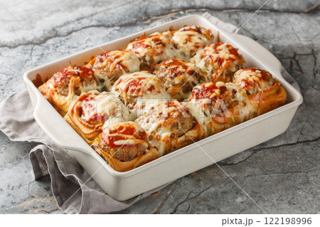 Hot sandwiches made from dinner rolls filled with meatballs, topped with tomato sauce and sprinkled with cheese close-up in a baking dish. horizontal Hot sandwiches made from dinner rolls filled with meatballs, topped with tomato sauce and sprinkled with cheese close-up in a baking dish. horizontal 122198996