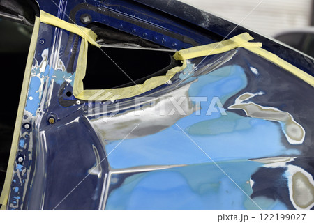 Close-Up of Car Being Repaired Showing Masked and Painted Bodywork. The surface is prepared with masking tape for precise painting or coating. Automotive maintenance and refinishing craftsmanship. 122199027