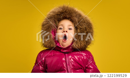 Portrait of little girl, child in pink warm winter coat yawning, feeling sleepy against yellow studio background Portrait of little girl, child in pink warm winter coat yawning, feeling sleepy against yellow studio background 122199529