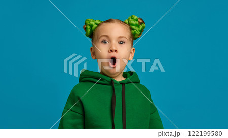 Portrait of cute little girl, child in green hoodie and braid buns hairstyle, expressing positive excitement and shock against blue studio background Portrait of cute little girl, child in green hoodie and braid buns hairstyle, expressing positive excitement and shock against blue studio background 122199580