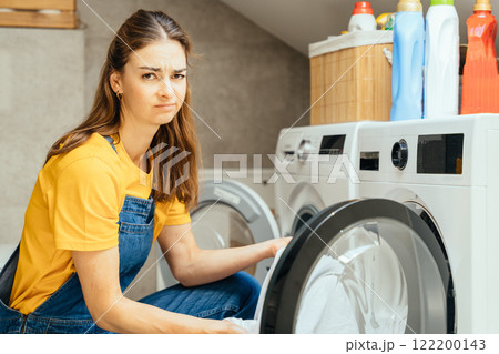 Female discouraged at laundry chore Tired woman is sitting on bathroom floor and looking at dirty clothes. 122200143