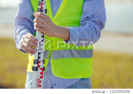 Worker is unfolding leveling rod on construction site. 122204109