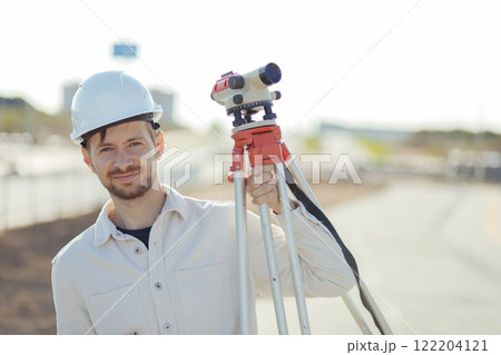 Engineer Surveyor Carries Tripod Level on shoulder. Walks at Construction Place 122204121