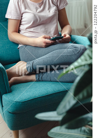 Young woman using mobile phone while sitting in cozy armchair 122204792