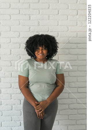 Laughing millennial African American woman with an afro hairstyle and good sense of humor smiling and laugh on brick wall at home background. Copy space. Happiness and good emotions concept Laughing millennial African American woman with an afro hairstyle and good sense of humor smiling and laugh on brick wall at home background. Copy space. Happiness and good emotions concept 122204835
