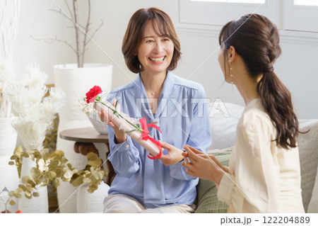 母の日　自宅のリビングでカーネーションとプレゼントを渡す若い女性と受け取る母親 122204889