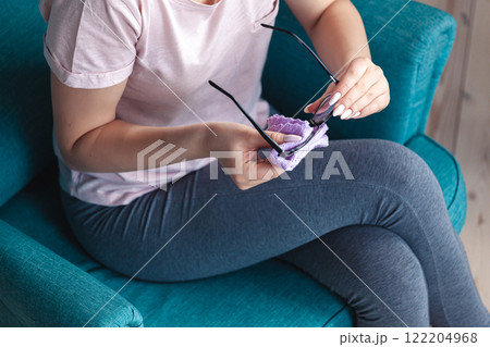 Young woman cleaning glasses with a napkin while sitting in a ch 122204968
