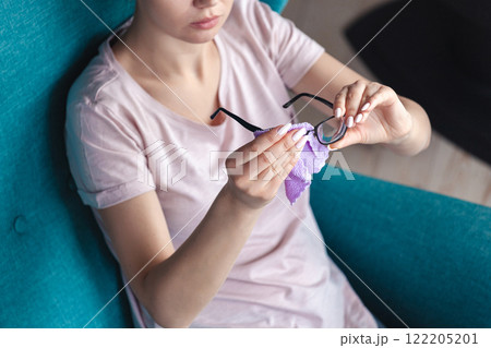 Young woman cleaning glasses with a napkin while sitting in a ch 122205201