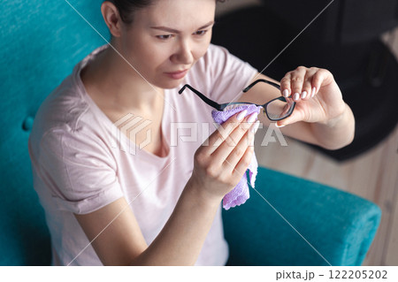 Young woman cleaning glasses with a napkin while sitting in a ch 122205202
