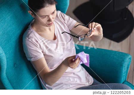 Young woman cleaning glasses with a napkin while sitting in a ch 122205203