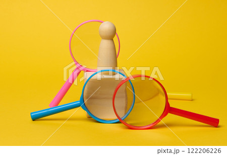 Wooden figurine on cube and plastic magnifying glass on yellow background, talent and employee search concept Wooden figurine on cube and plastic magnifying glass on yellow background, talent and employee search concept 122206226