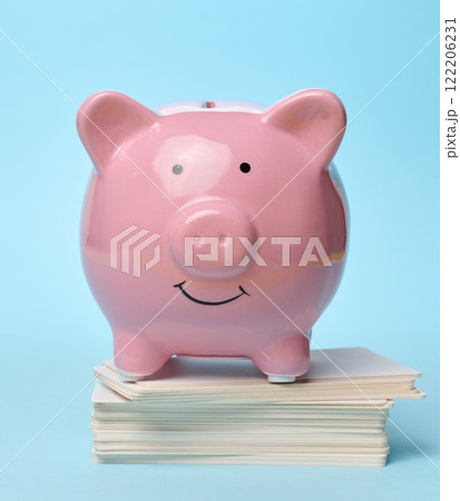 Ceramic piggy bank stands on a stack of business cards on a blue background 122206231