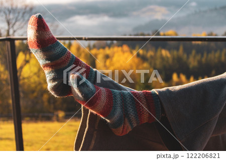 Woman crossed legs in knitted socks on autumn mountains background. Feet in striped socks on sunny autumn forest background. Handmade knitted fashion. Cozy lifestyle concept. Warm clothing outdoors. Woman crossed legs in knitted socks on autumn mountains background. Feet in striped socks on sunny autumn forest background. Handmade knitted fashion. Cozy lifestyle concept. Warm clothing outdoors. 122206821