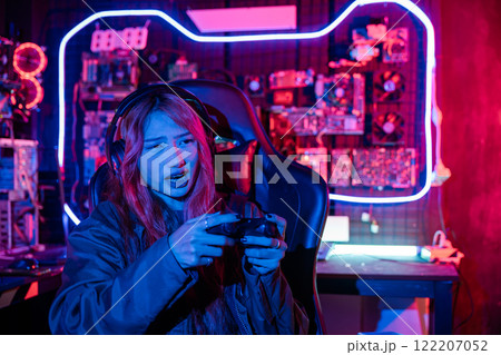 Woman wear gaming headphones playing esports games console gaming room, Gamer using joystick controller for race tournament plays online video game with computer neon lights 122207052