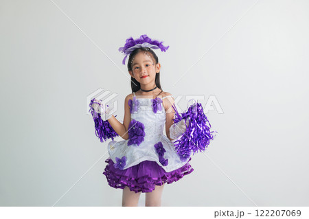 Cheerful young cheerleader girl in a purple and white outfit, holding pom-poms. Energetic studio shot on a white background, full of joy and excitement. cheerleader kid 122207069