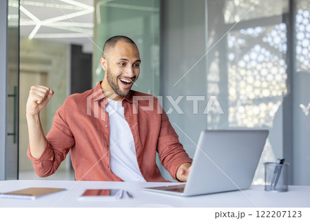 Joyful and successful man celebrating successful achievement results at workplace, businessman in casual clothes received winning and triumphant news online, uses laptop. 122207123