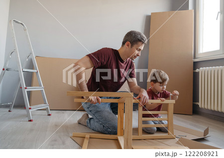 Smiling dad teaches his little son how to use tools while assembling furniture together 122208921