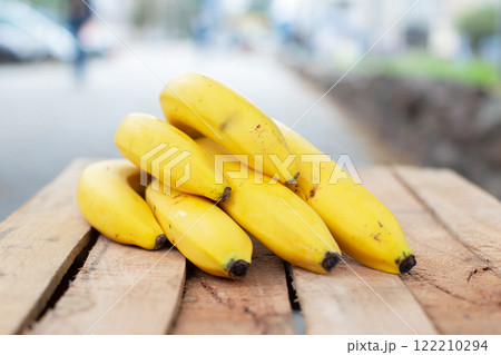 A yellow branch of ripe bananas lies on a wooden bench. A yellow branch of ripe bananas lies on a wooden bench. 122210294