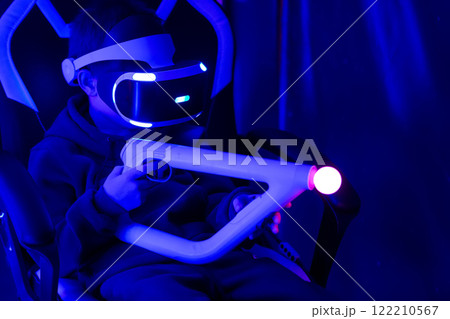 A boy is playing a video game with a controller. The controller is white and has a red light on it. The room is dark and the boy is sitting in a chair A boy is playing a video game with a controller. The controller is white and has a red light on it. The room is dark and the boy is sitting in a chair 122210567