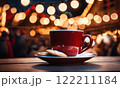 Merry Christmas and Happy Holidays. A cup of hot drink and cookies with background of the lights of Christmas market. Cup of coffee on the window sill. Bright lights of the city hristmas background. 122211184