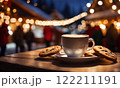 Merry Christmas and Happy Holidays. A cup of hot drink and cookies with background of the lights of Christmas market. Cup of coffee on the window sill. Bright lights of the city hristmas background. 122211191