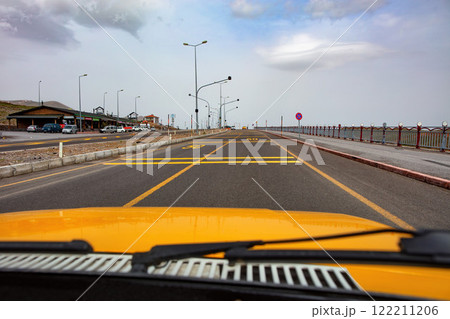 Journey down a coastal road with yellow car and distant mountains under a cloudy sky 122211206