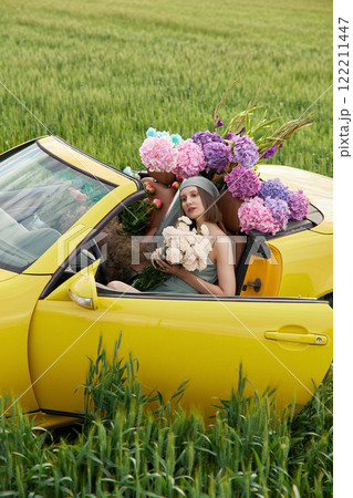 A young girl is sitting in a yellow convertible surrounded by bright flowers 122211447