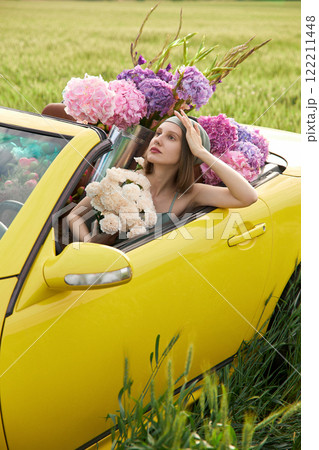 A young girl is sitting in a yellow convertible surrounded by bright flowers 122211448