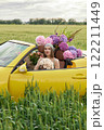 A young girl is sitting in a yellow convertible surrounded by bright flowers 122211449