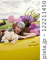 A young girl is sitting in a yellow convertible surrounded by bright flowers 122211450