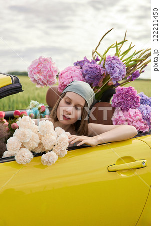 A young girl is sitting in a yellow convertible surrounded by bright flowers 122211450