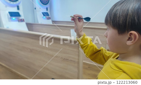 Cute preschool age boy playing darts indoors. Happy child having fun with darts board winning the game. Concept of self-confidence, nurturing Cute preschool age boy playing darts indoors. Happy child having fun with darts board winning the game. Concept of self-confidence, nurturing 122213060