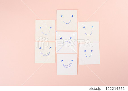 Crossed out sad face surrounded by happy smileys on paper cards on pink background. Crossed out sad face surrounded by happy smileys on paper cards on pink background. 122214251