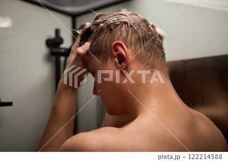 A person is enjoying a refreshing shower while using shampoo in a modern bathroom setting A person is enjoying a refreshing shower while using shampoo in a modern bathroom setting 122214588