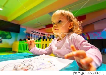 A cheerful child exploring creativity through coloring in a lively indoor playground. A cheerful child exploring creativity through coloring in a lively indoor playground. 122214736