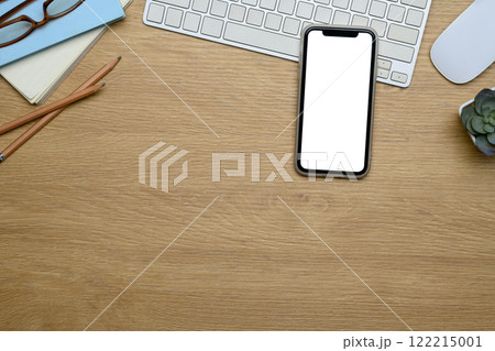 Smartphone, keyboard, glasses, and small succulent plant on wooden desk surface 122215001