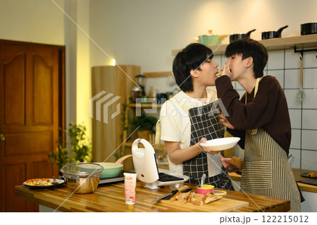 Loving male gay couple preparing a delicious breakfast at counter in warm kitchen Loving male gay couple preparing a delicious breakfast at counter in warm kitchen 122215012