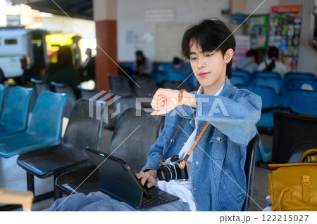 Young traveler checking time on his wristwatch while sitting at a bus station 122215027