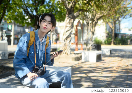 Male traveler sitting on a bench in public park and using smartphone Male traveler sitting on a bench in public park and using smartphone 122215030