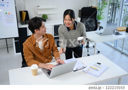 Smiling female colleague sharing ideas over laptop with her coworker in the office 122215033
